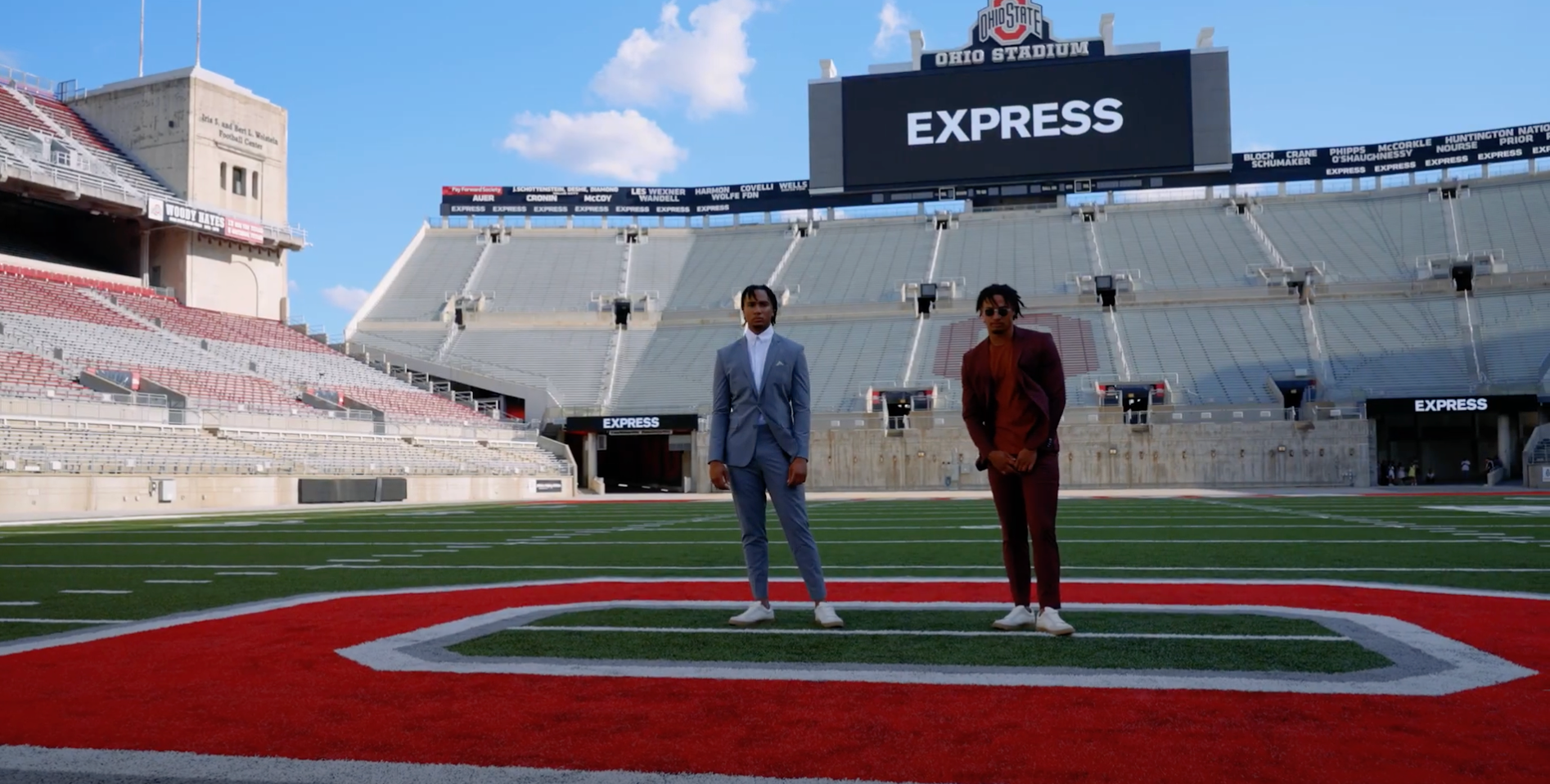 two athletes on a football field wearing suits with an "Express" sign in the background