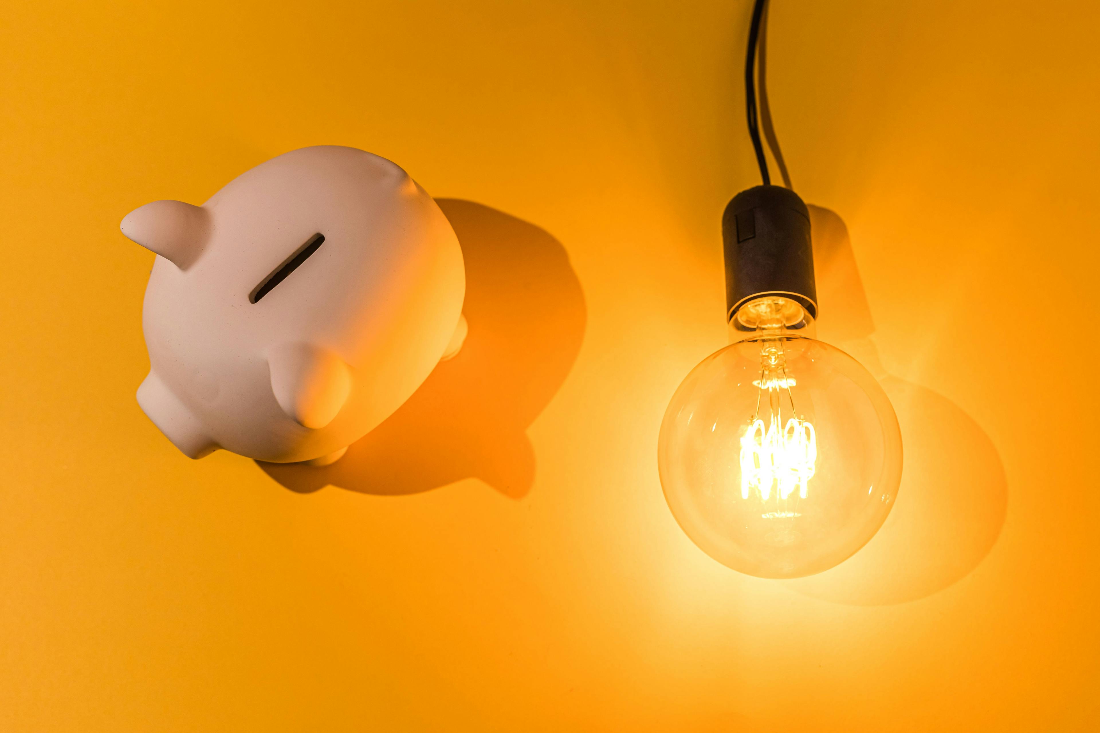piggy bank next to a light bulb on a yellow background