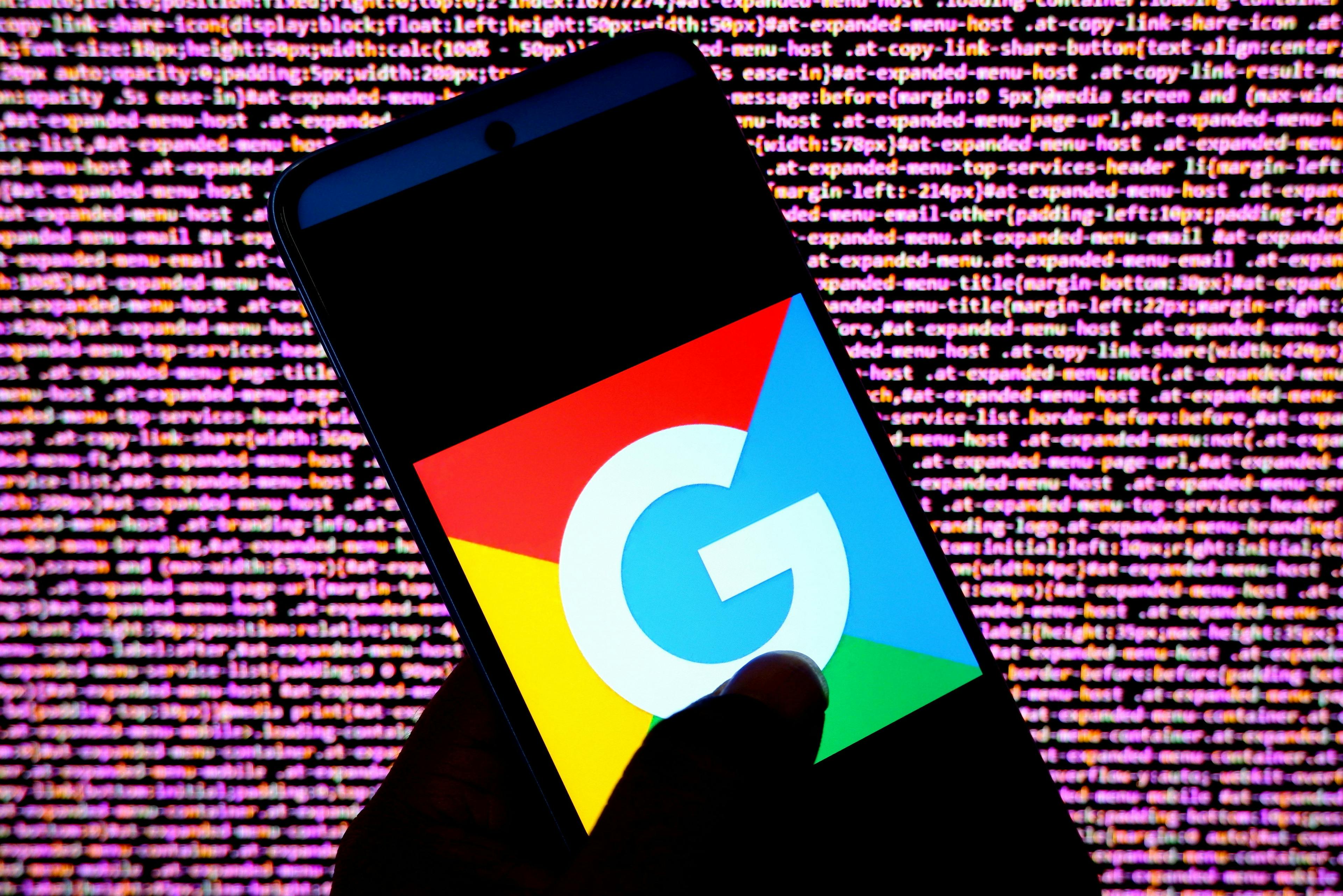 a Google logo appears on a silhouette of a smart phone in front of a wall of computer code